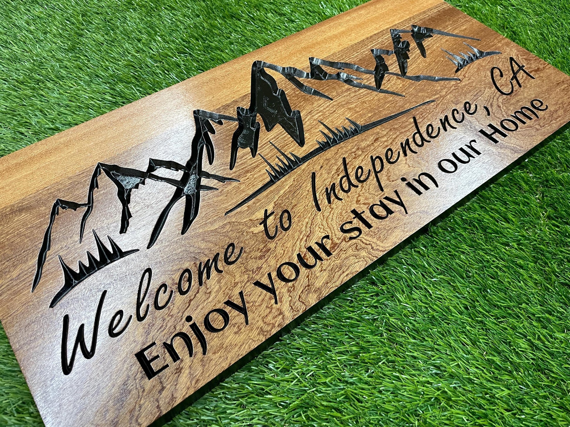 a wooden sign with a mountain landscape design and text that reads "Welcome to Independence, CA Enjoy your stay in our Home".