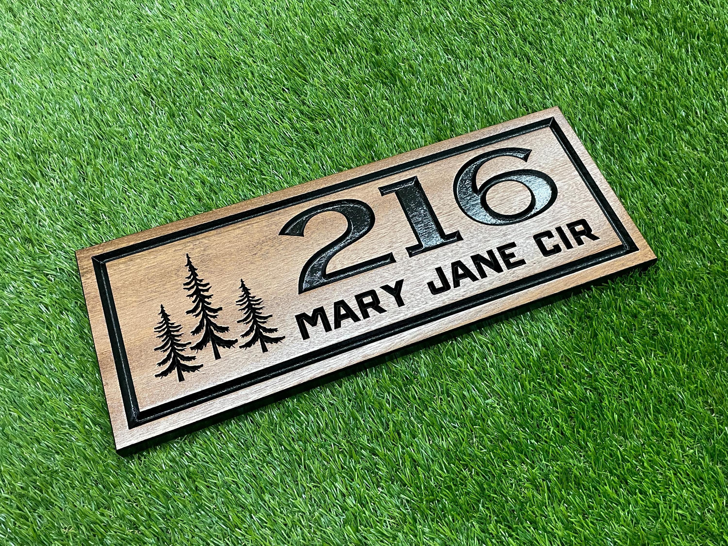 A wooden house number sign with the number "216" and the text "MARY JANE CIR" printed on it, placed on a grassy surface.