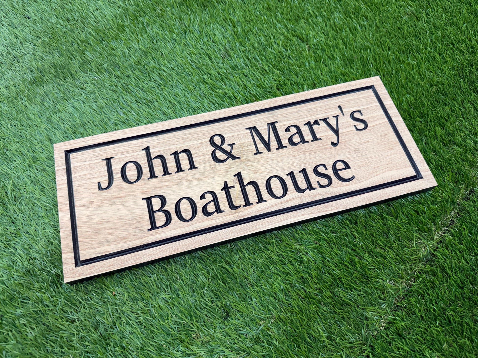 A wooden sign with the text "John & Mary's Boathouse" on it, placed on a grassy surface.