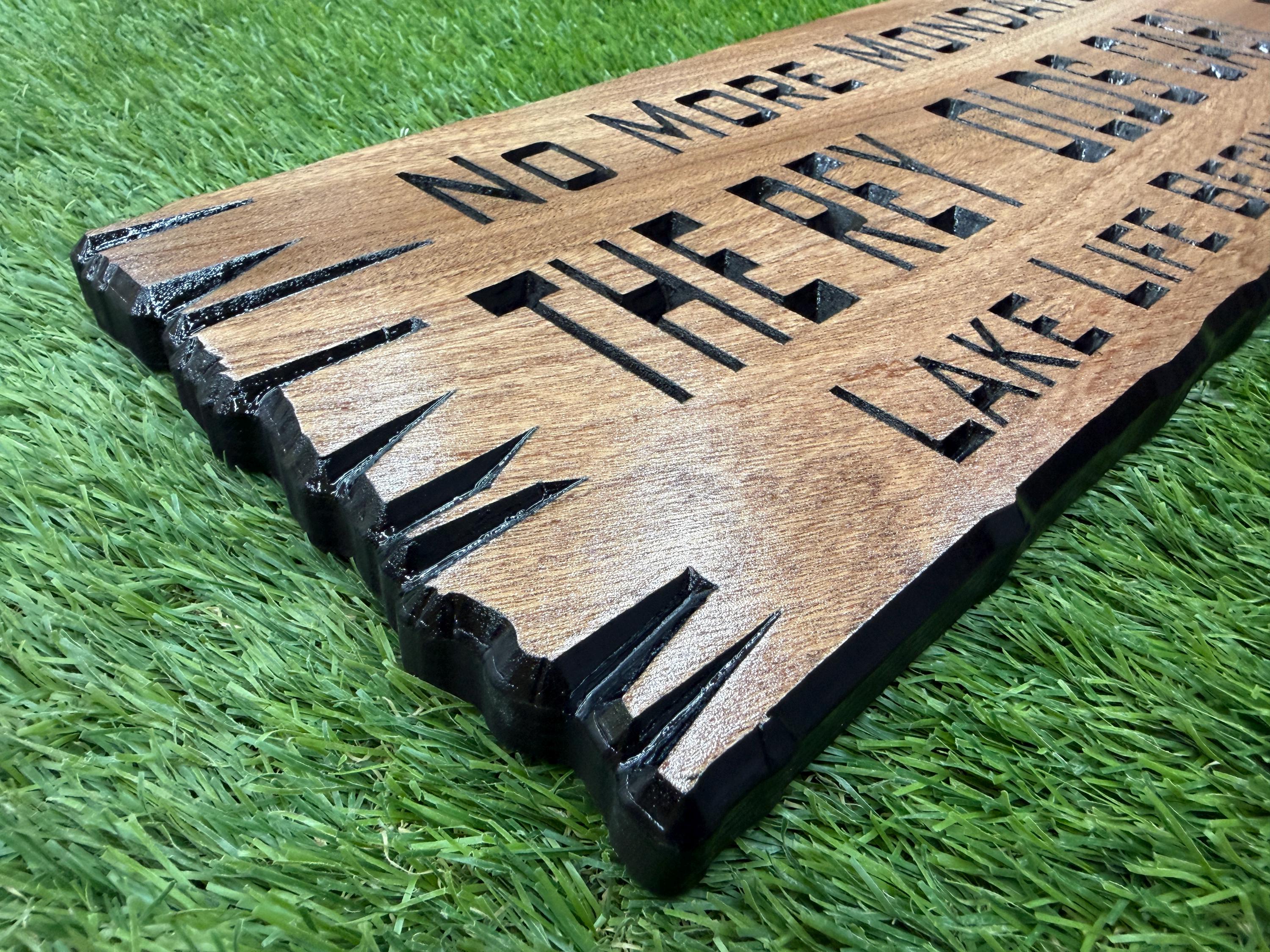 a wooden sign with the text "NO MORE MONTES" carved into it, placed on a grassy surface.