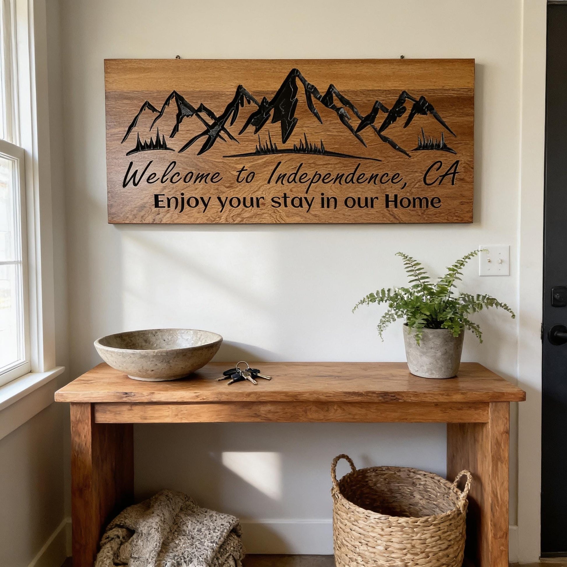 a wooden table with a bowl, a plant, and a woven basket, along with a wooden sign that reads "Welcome to Independence, CA Enjoy your stay in our Home".