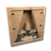 A wooden coin bank with a nameplate inside, containing various coins.