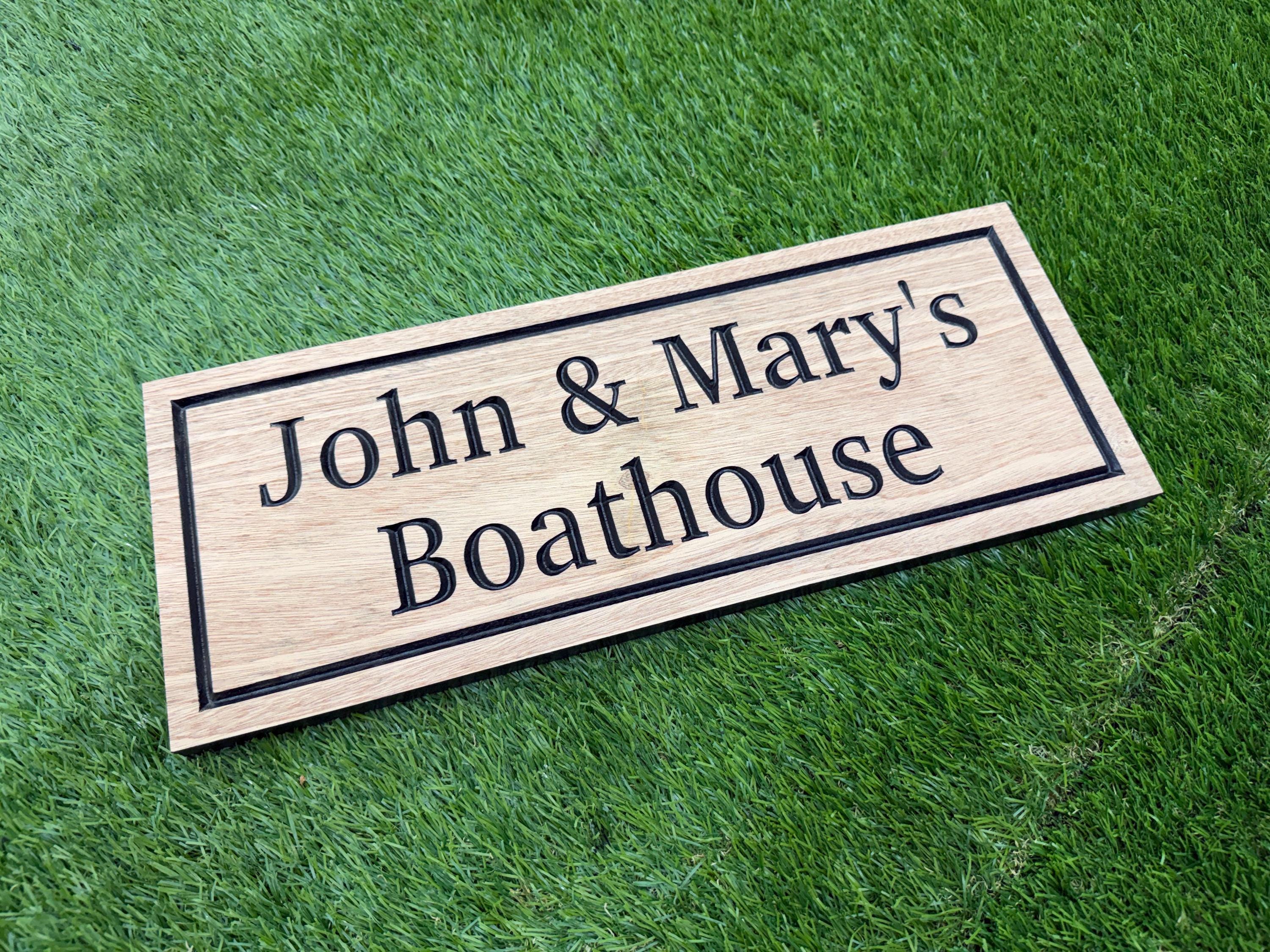 A wooden sign with the text "John & Mary's Boathouse" on it, placed on a grassy surface.