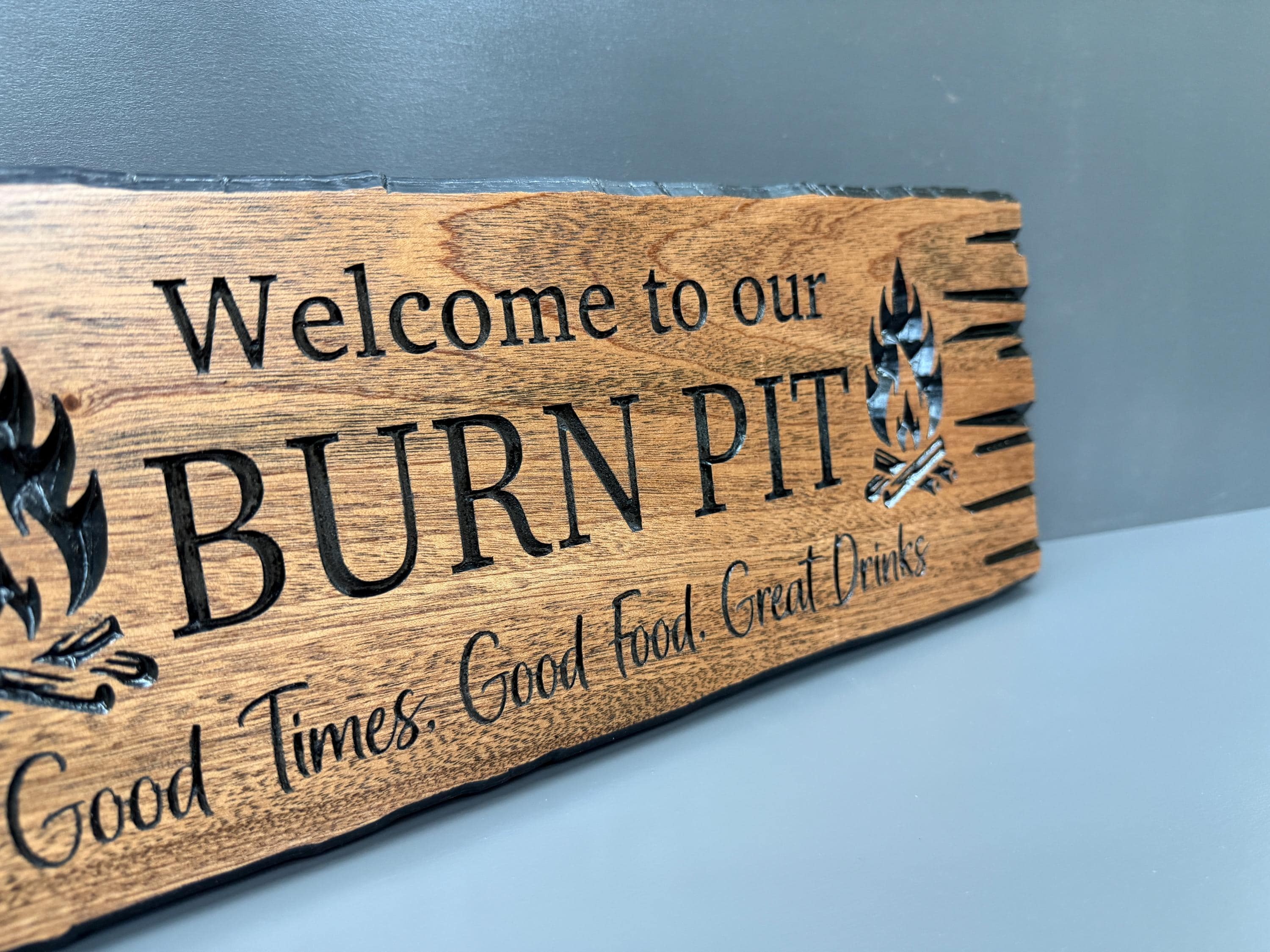A wooden sign with the text "Welcome to our BURN PIT" and "Good Times. Good Food. Great Drinks" carved into it.