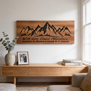 a wooden console table with a framed photo, a vase with greenery, and a wooden wall art depicting mountains. The wall art has the text "With Love Comes Adventure Hunter & Alyssa Friend 9-7-2024" written on it.