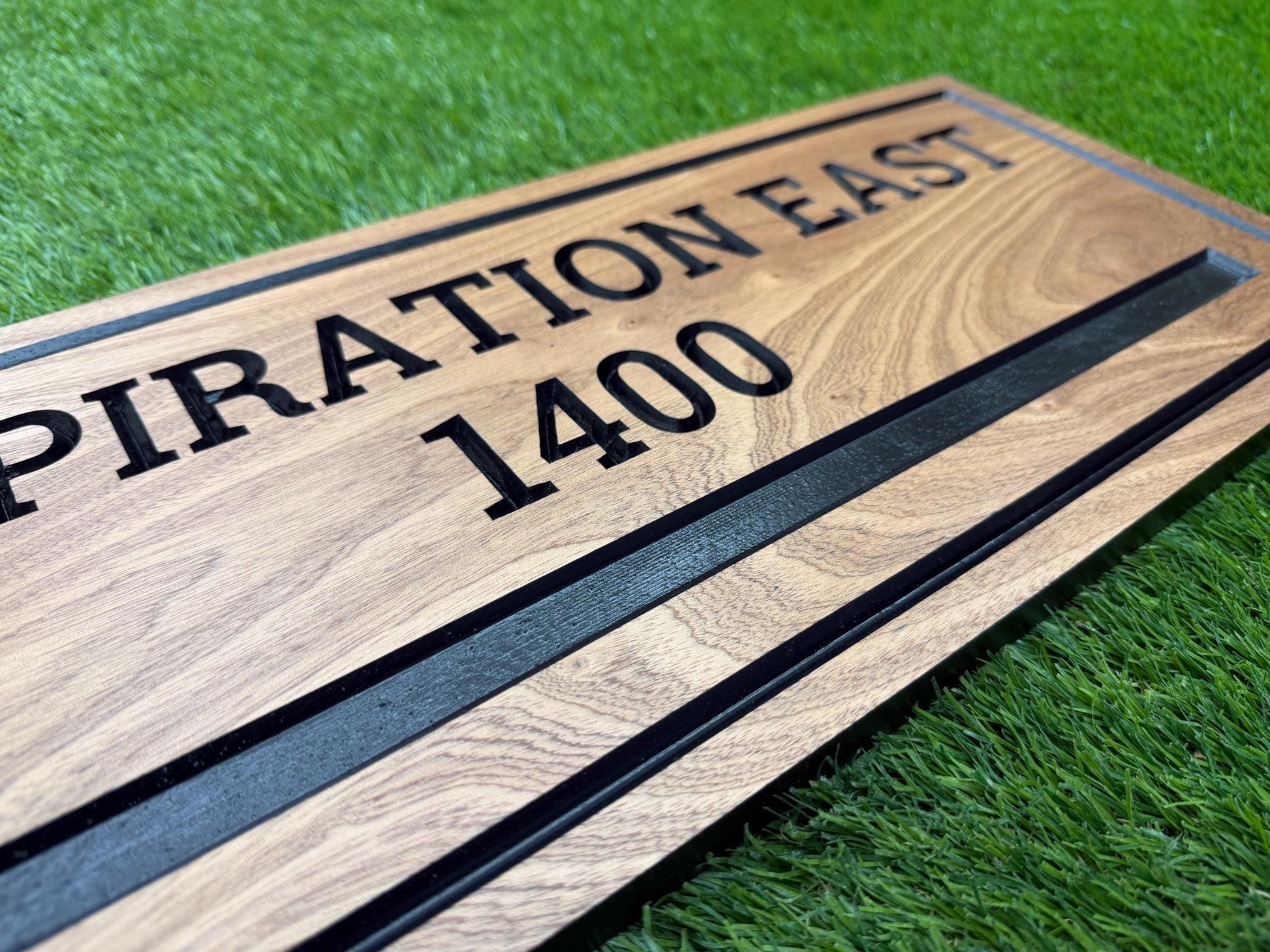A wooden sign with the text "SPIRATION EAST 1400" printed on it, placed on a grassy surface.