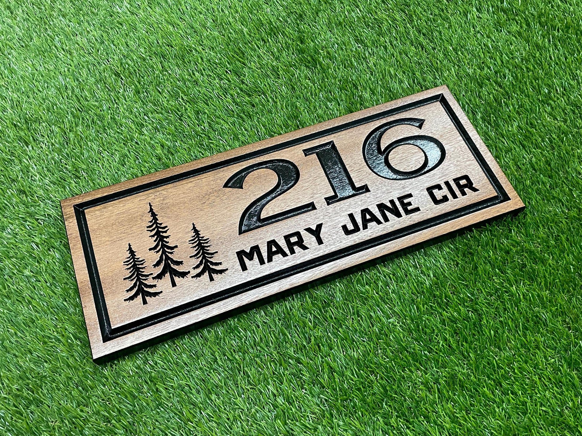 A wooden house number sign with the number "216" and the text "MARY JANE CIR" printed on it, placed on a grassy surface.