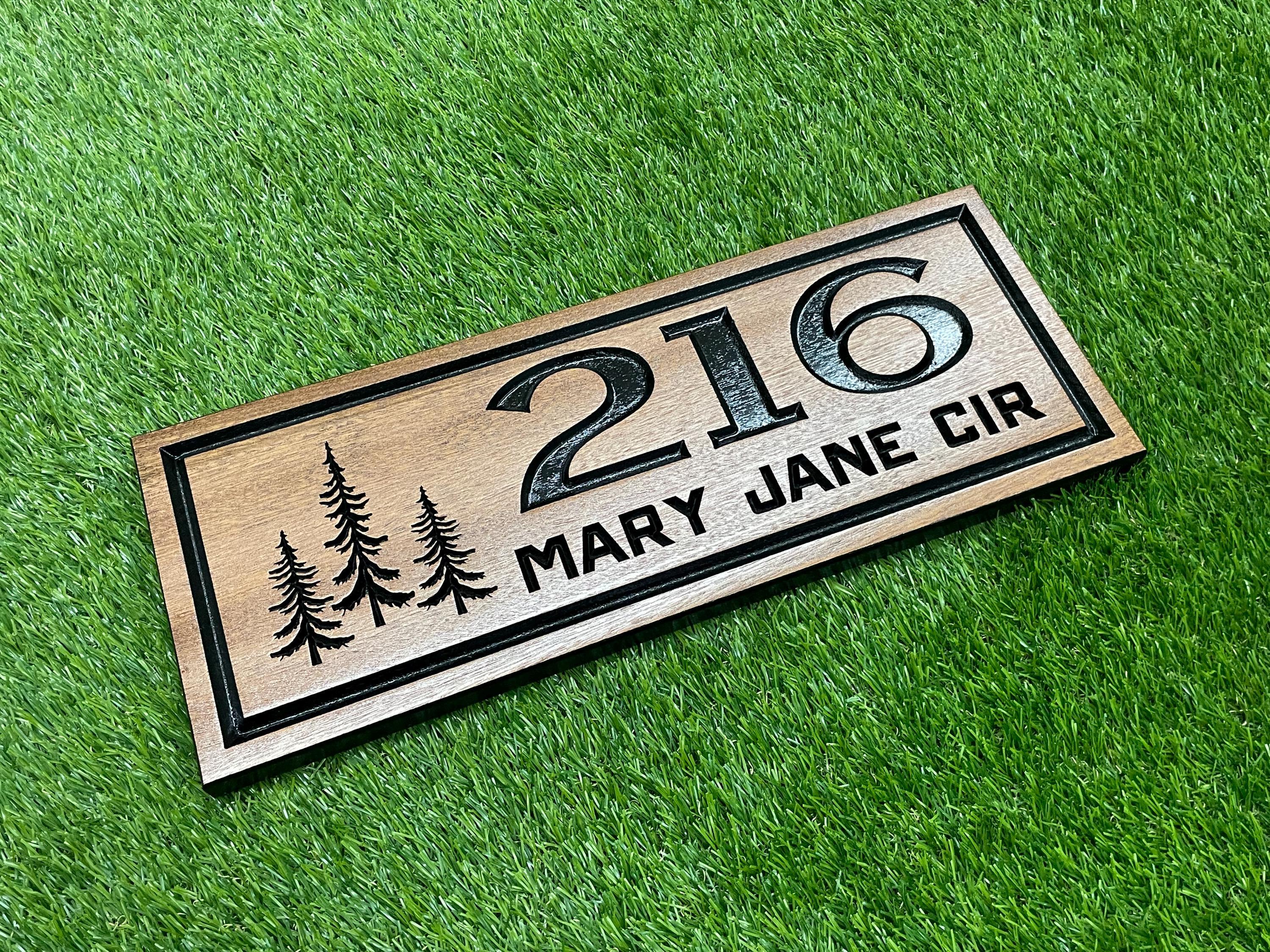 A wooden house number sign with the number "216" and the text "MARY JANE CIR" printed on it, placed on a grassy surface.