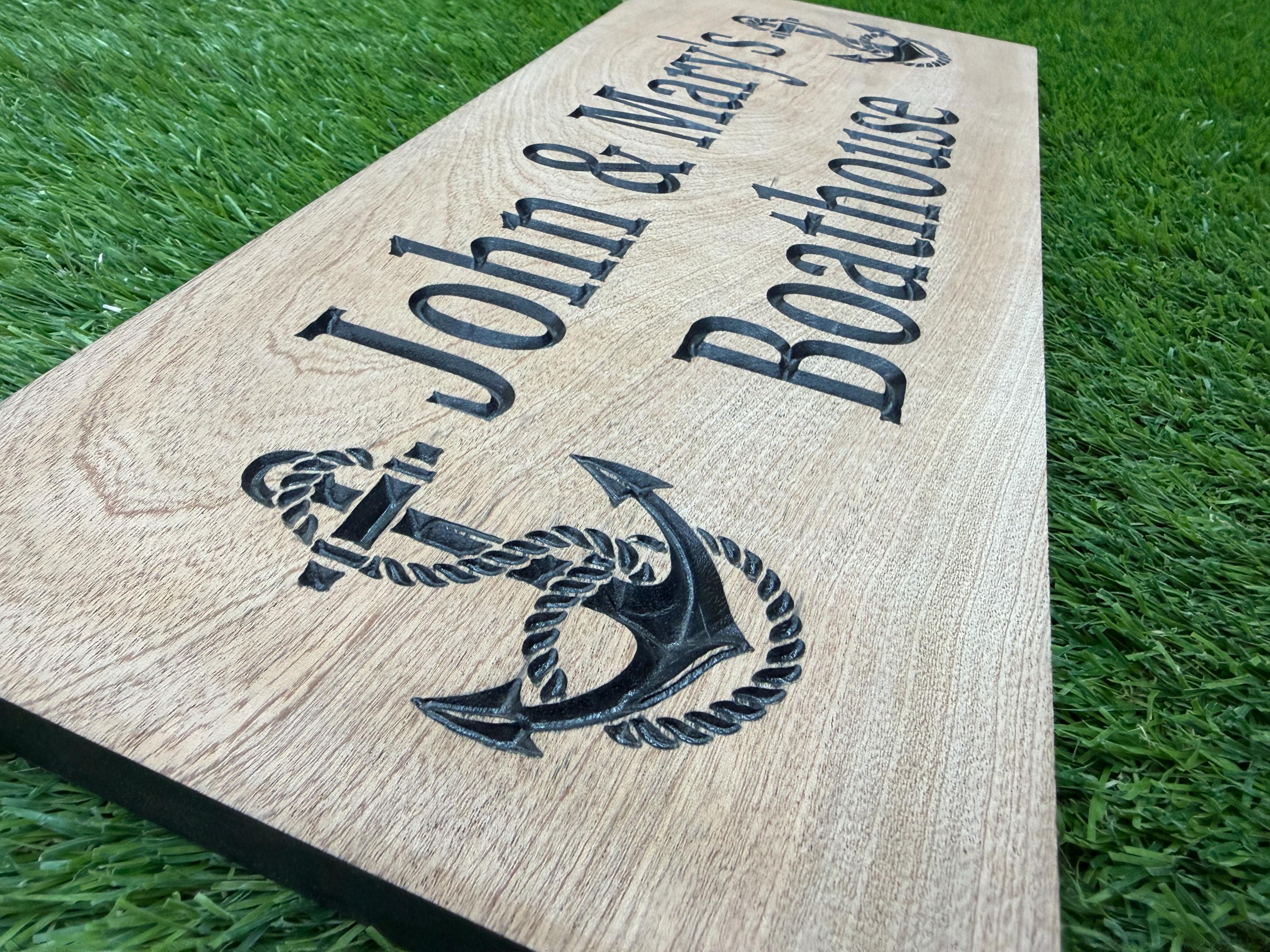 A wooden sign with the name "John & Mary's Boathouse" carved into it, featuring an anchor symbol.