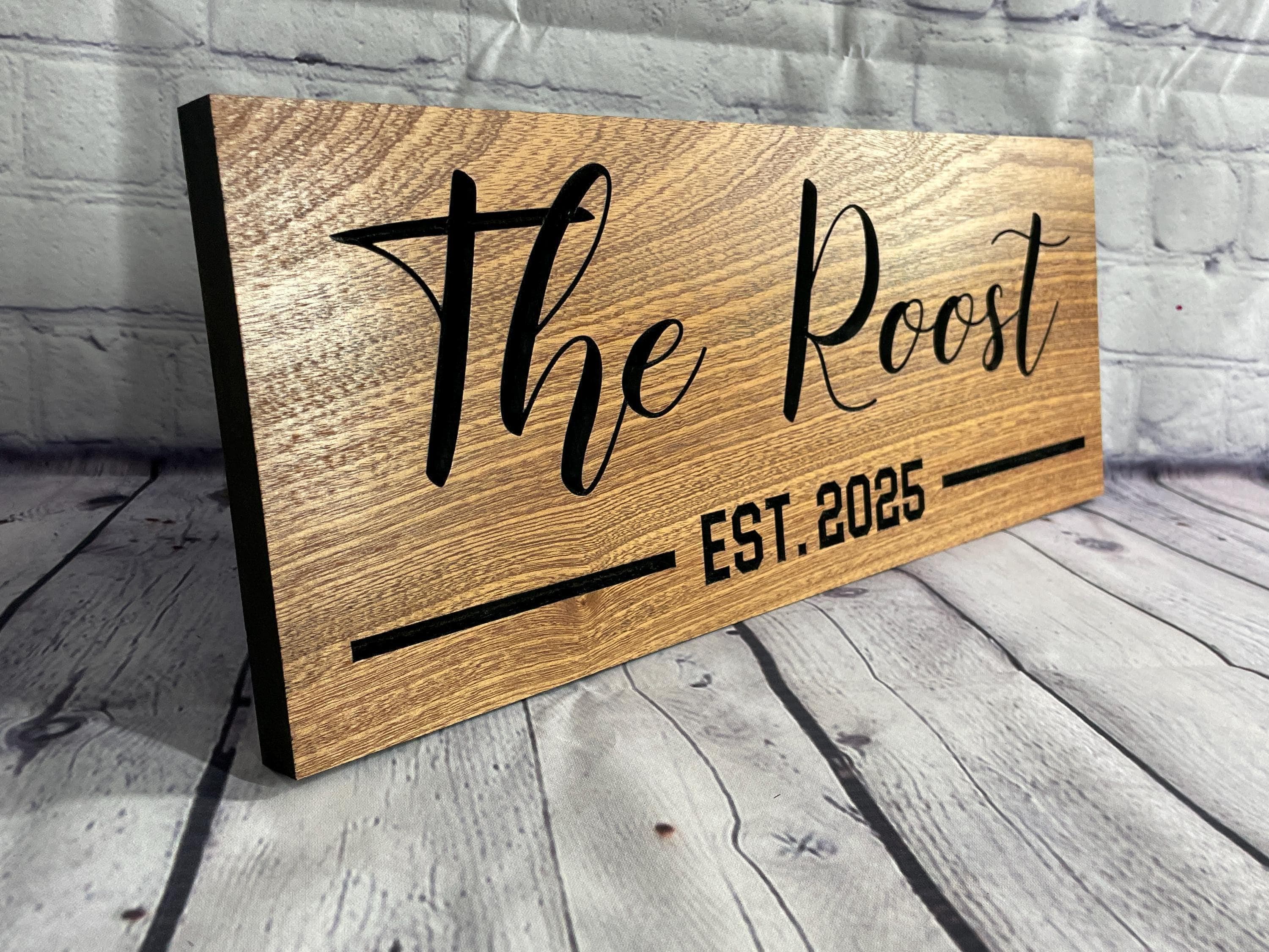 A wooden sign with the name "The Roost" and the year "EST. 2025" printed on it.