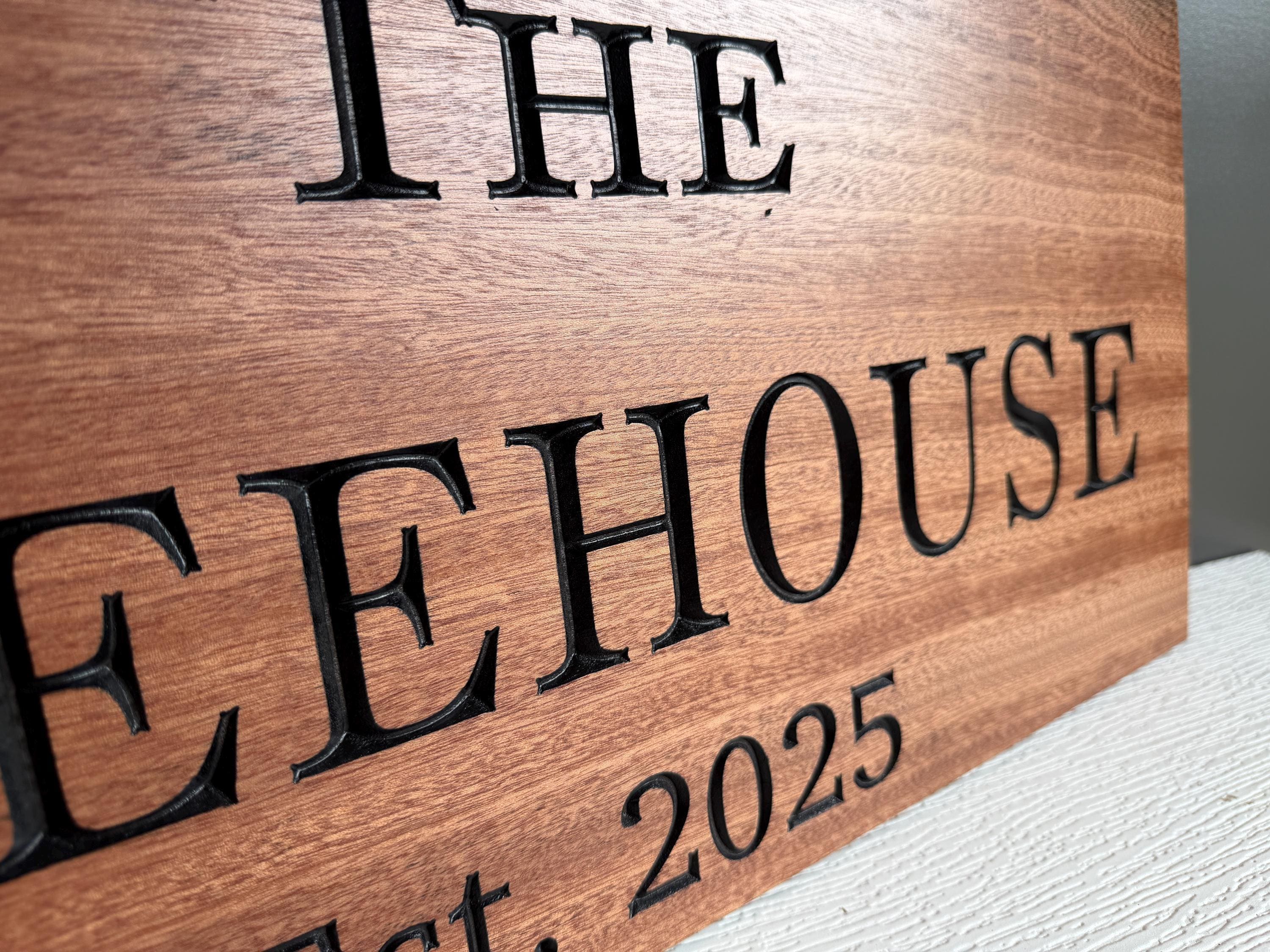 A wooden sign with the text "THE EHOUSE" and "EST. 2025" carved into it.