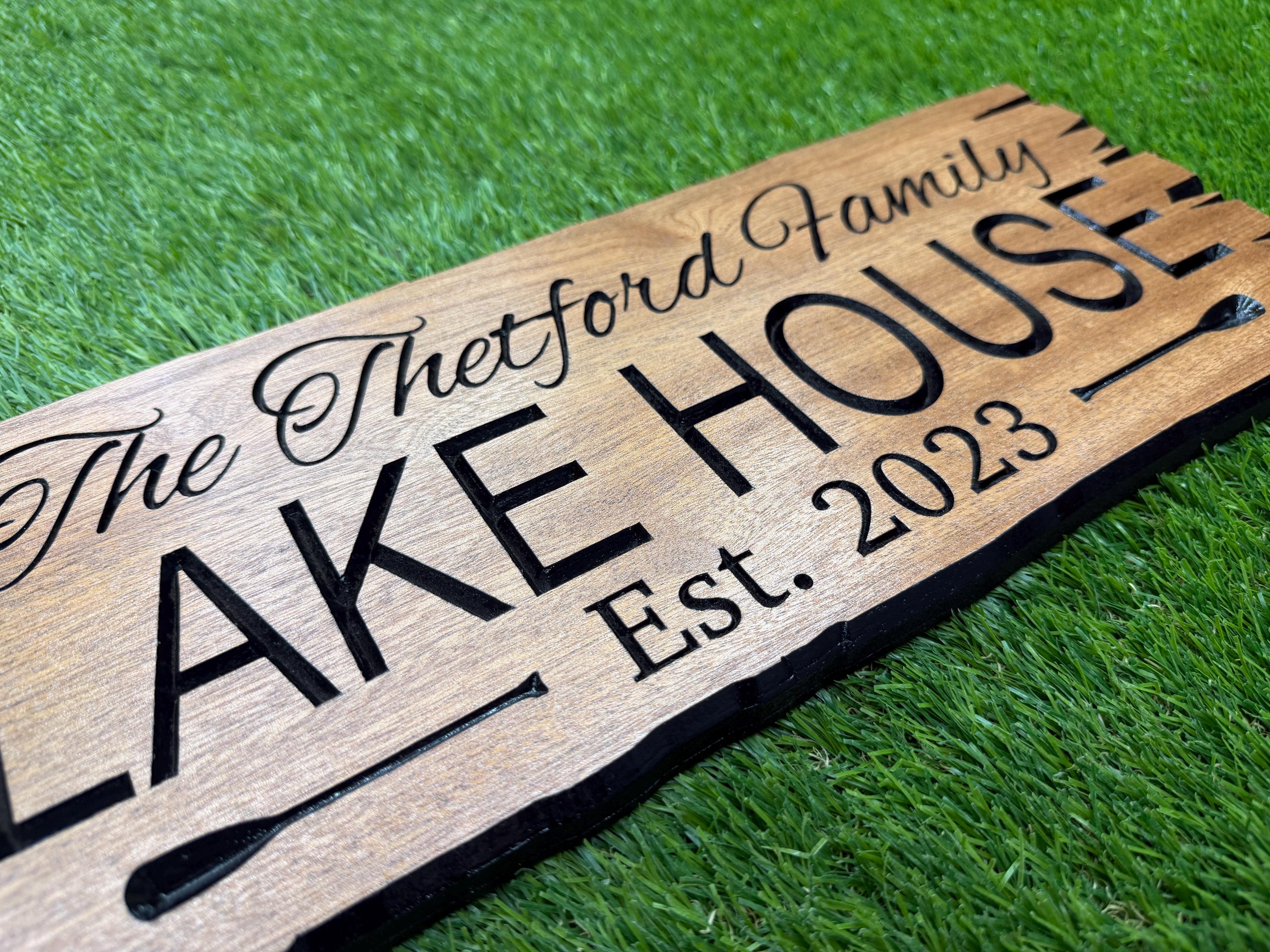 A wooden sign with the text "The Buttermilk House" and "Est. 2023" carved into it, placed on a grassy surface.