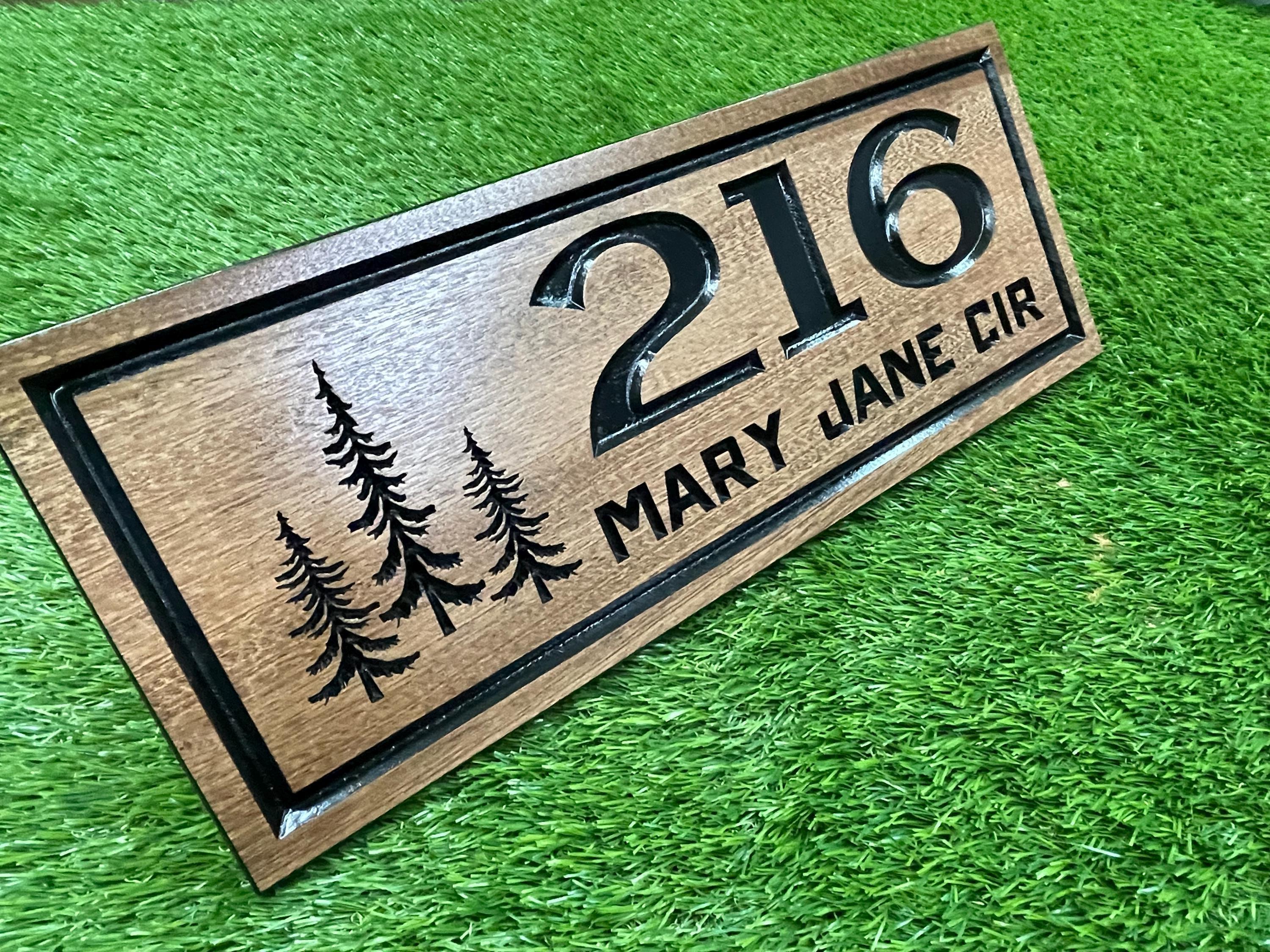 A wooden house number sign with the number "216" and the names "Mary Jane Cir" printed on it, placed on a grassy surface.