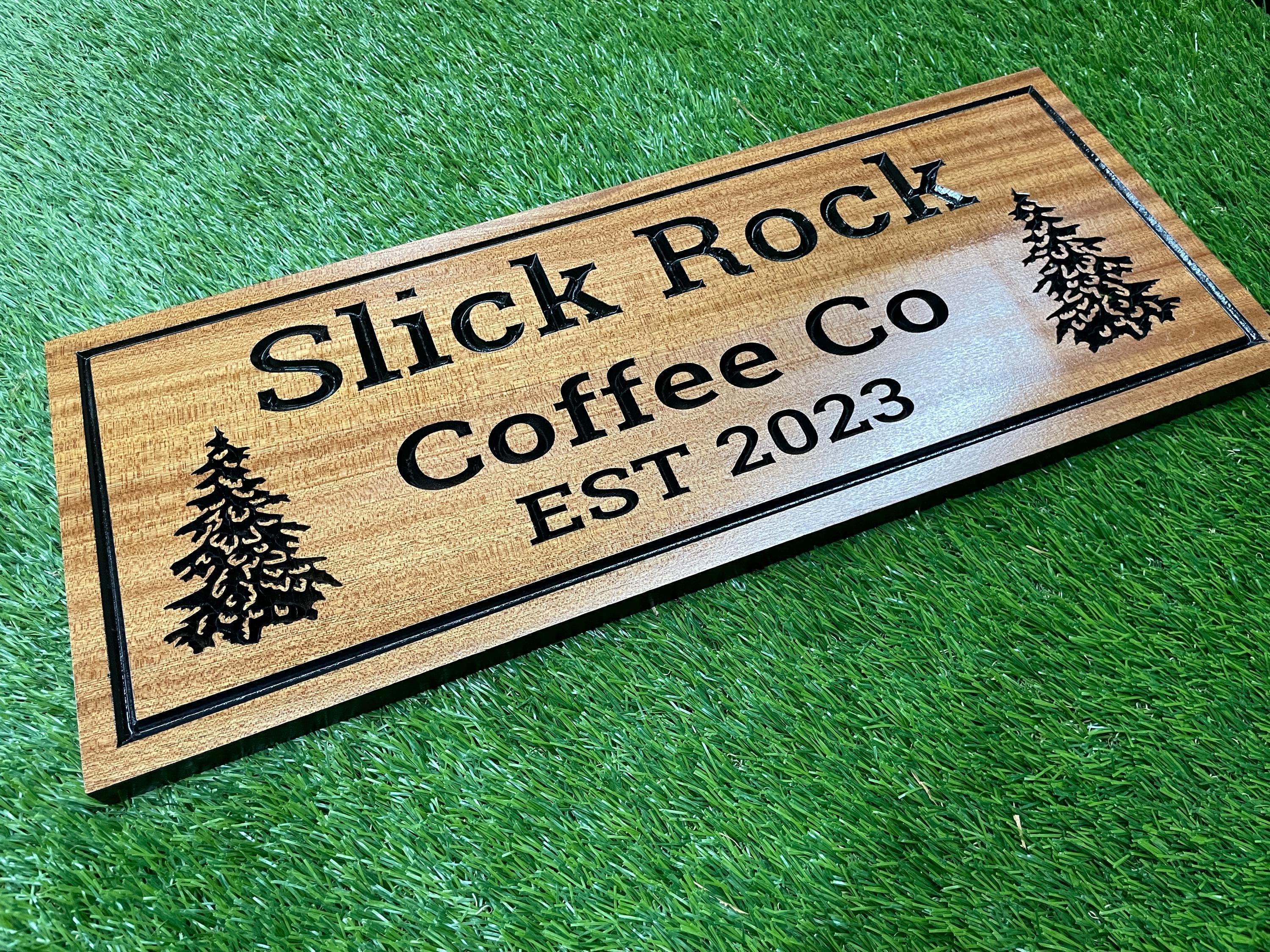 A wooden sign for "Slick Rock Coffee Co" with a forest-like design on the left side, placed on a green surface.