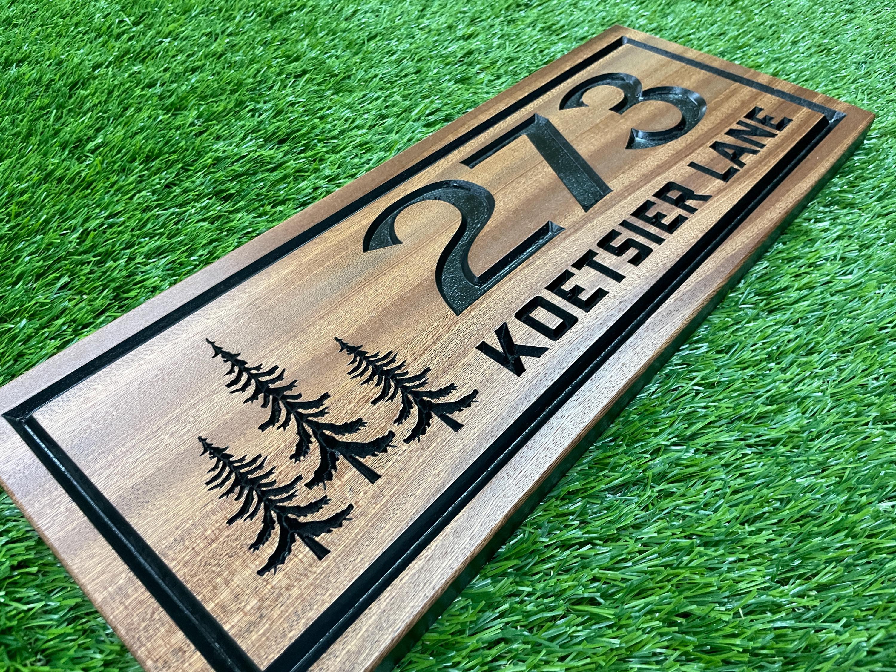 A wooden house number sign with the number "273" and the name "Koeitsier Lane" printed on it, placed on a grassy surface.
