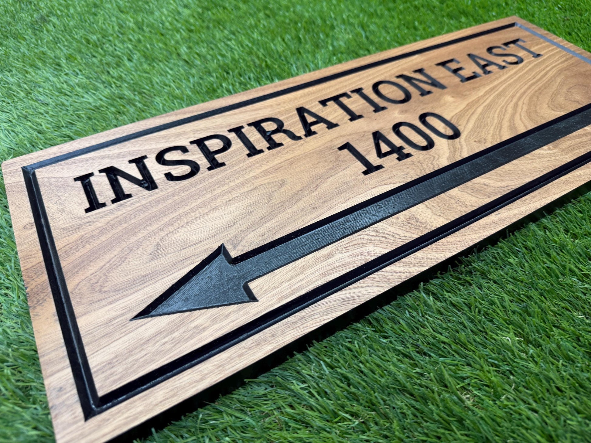 A wooden sign with the text "INSPIRATION EAST 1400" and an arrow pointing to the right, placed on a grassy surface.