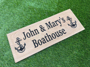 A wooden sign with the text "John & Mary's Boathouse" and two anchor symbols is placed on a grassy surface.