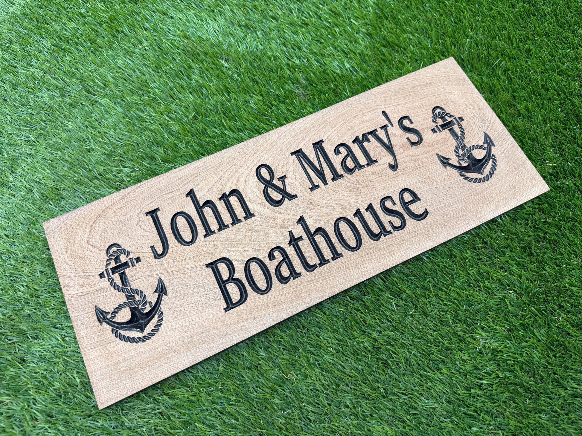 A wooden sign with the text "John & Mary's Boathouse" and two anchor symbols is placed on a grassy surface.