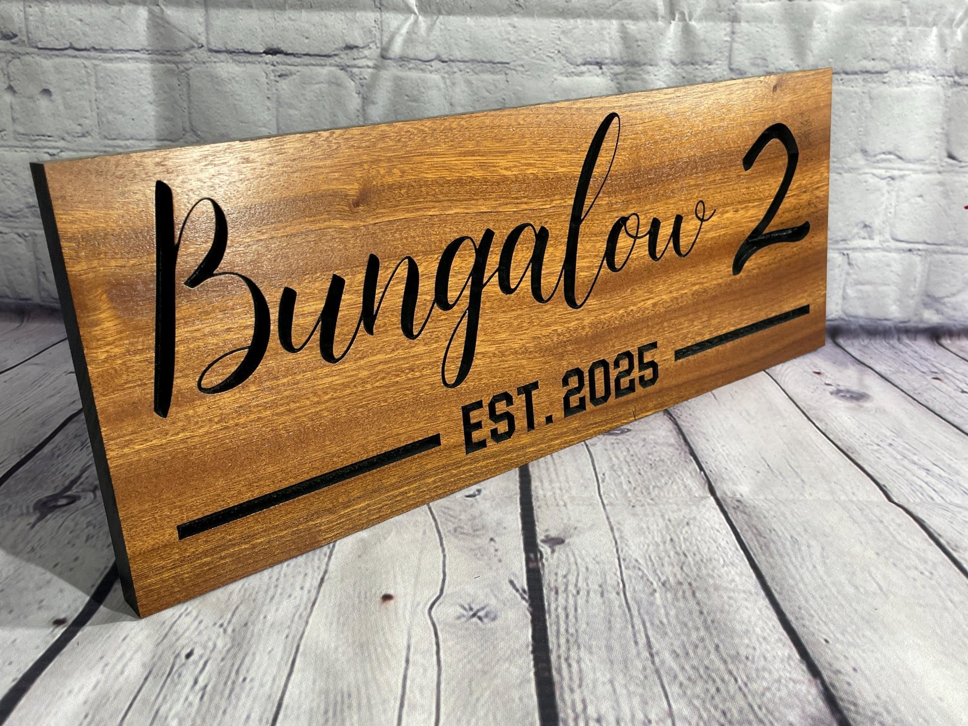 A wooden sign with the name "Bungalow 2" and the year "EST. 2025" printed on it.