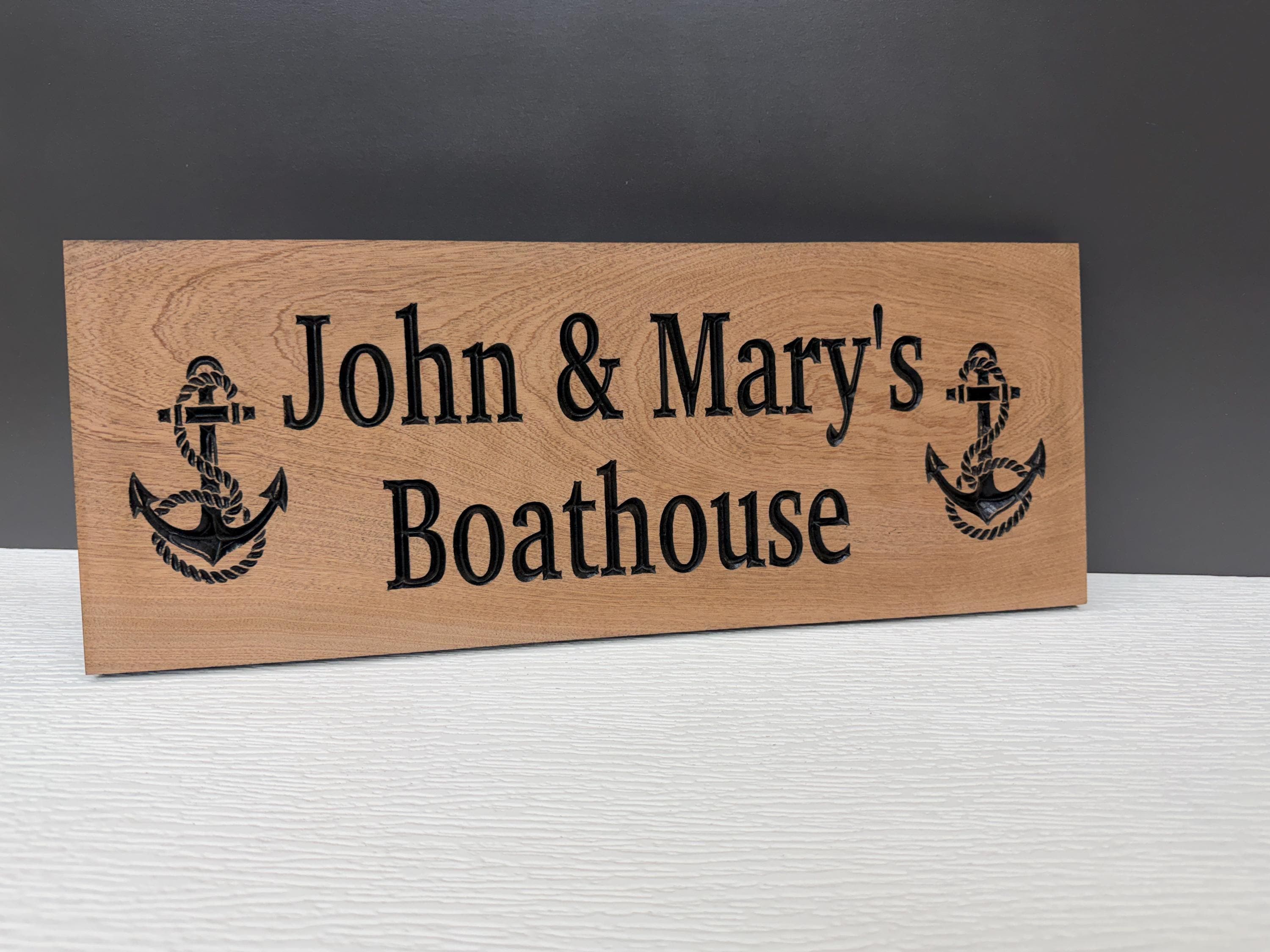 A wooden sign with the text "John & Mary's Boathouse" and two anchor symbols on it.