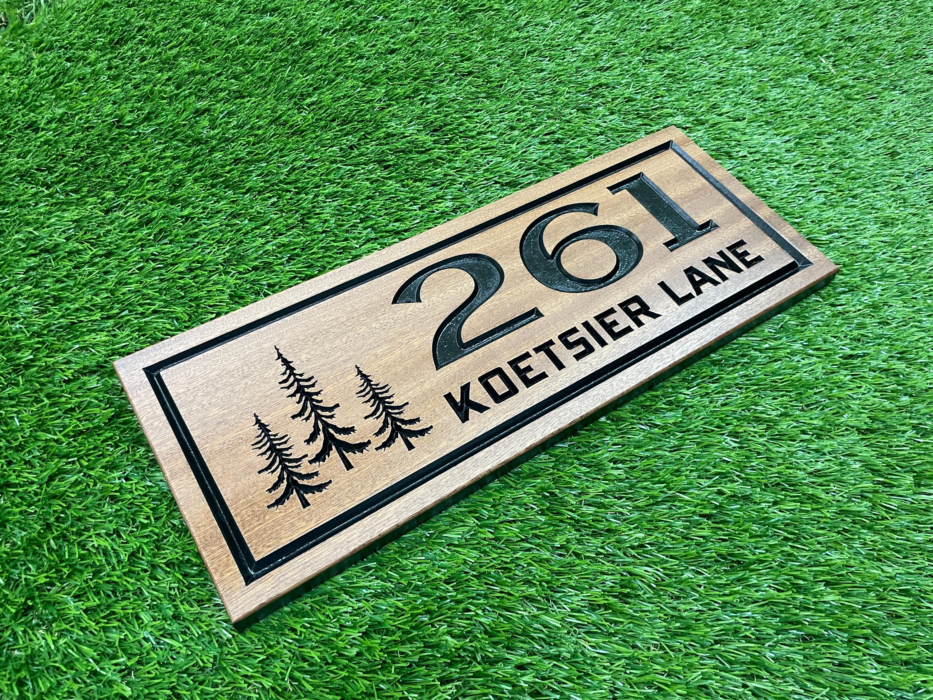 A wooden house number sign with the number "261" and the name "KOETSIER LANE" printed on it, placed on a grassy surface.