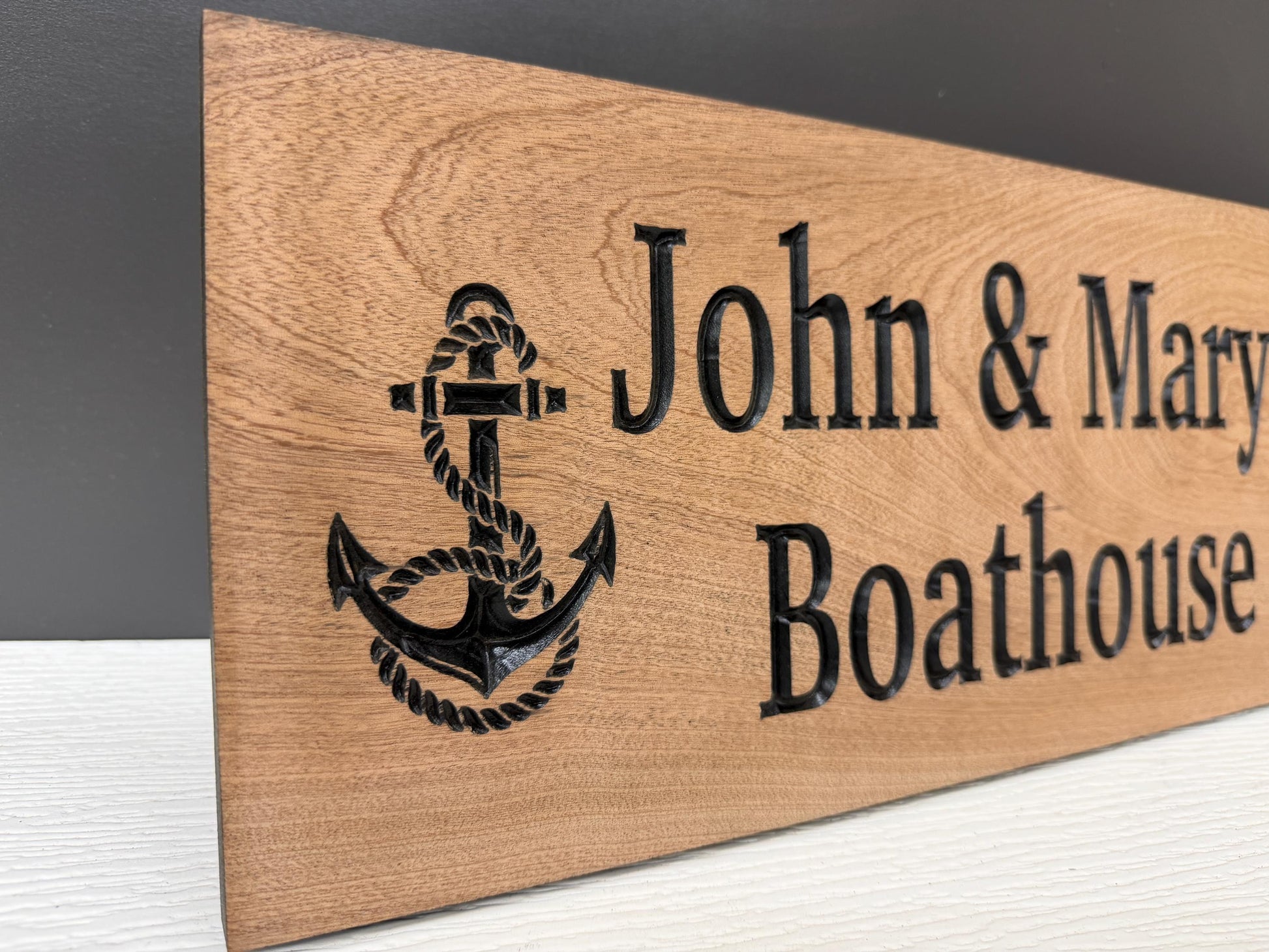 A wooden sign with the name "John & Mary Boathouse" carved into it, featuring an anchor symbol.