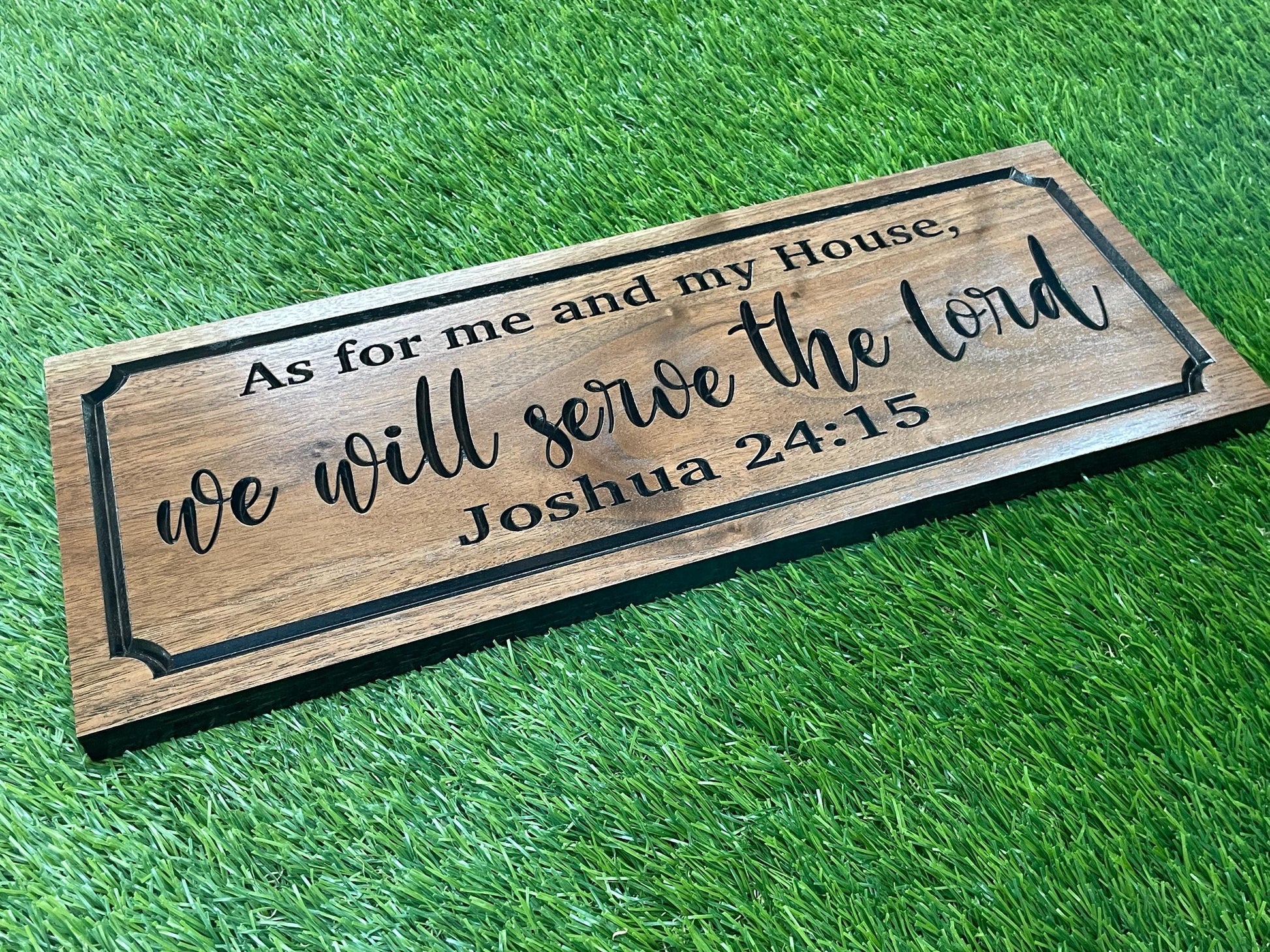 A wooden sign with the text "As for me and my House, we will serve the Lord Joshua 24:15" printed on it, placed on a grassy surface.