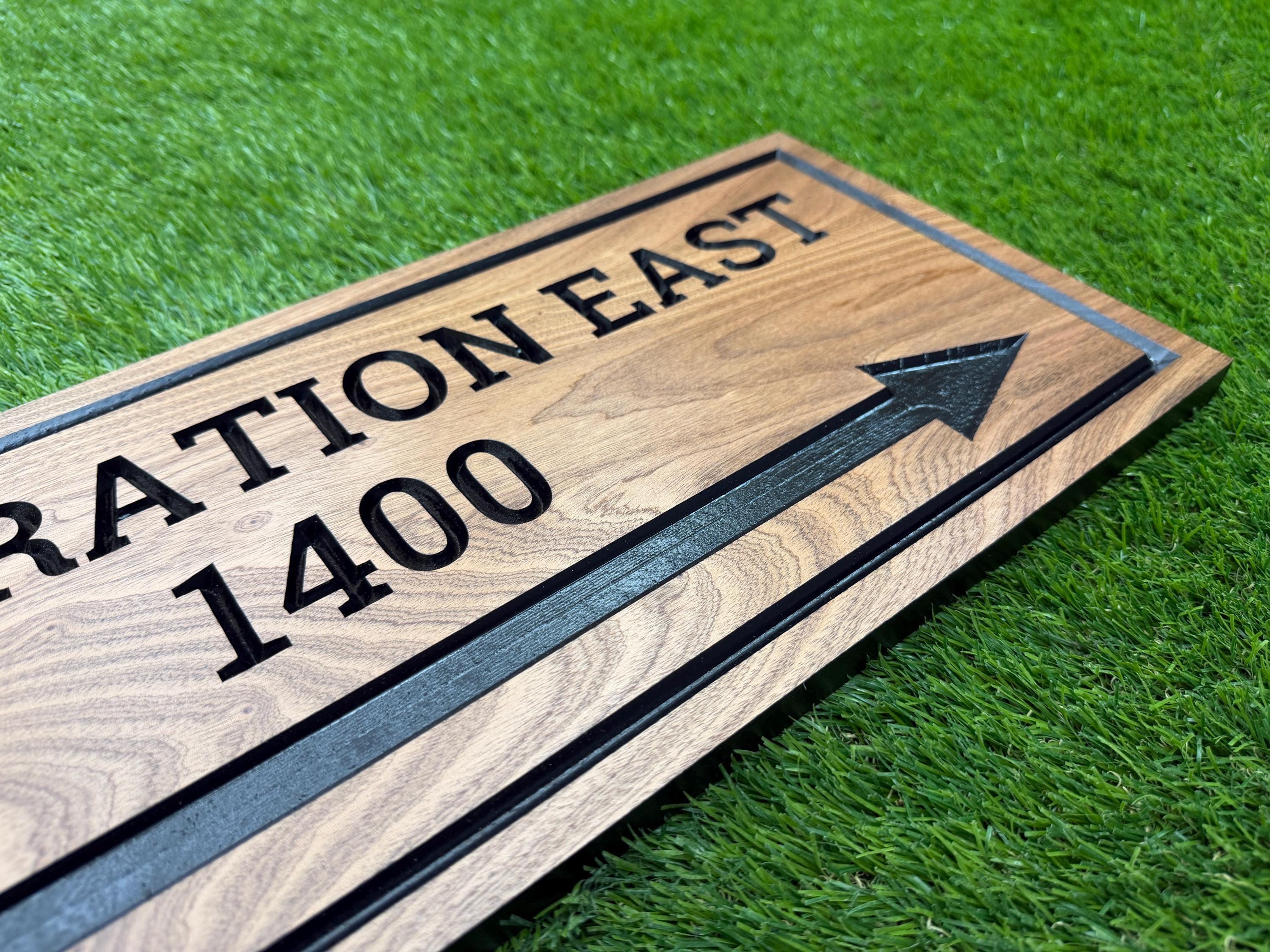 A wooden sign with black text and an arrow pointing to the right, placed on a grassy surface.