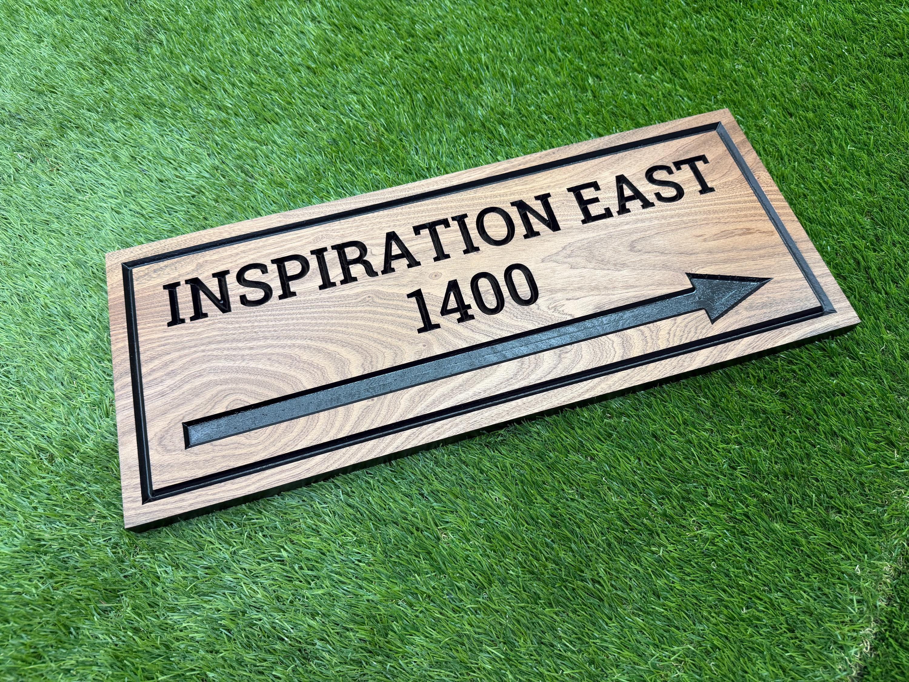 A wooden sign with the text "INSPIRATION EAST 1400" and an arrow pointing to the right, placed on a grassy surface.