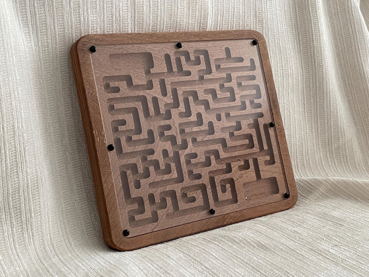 A wooden maze game board with a clear plastic maze pattern on it, placed on a white fabric background.