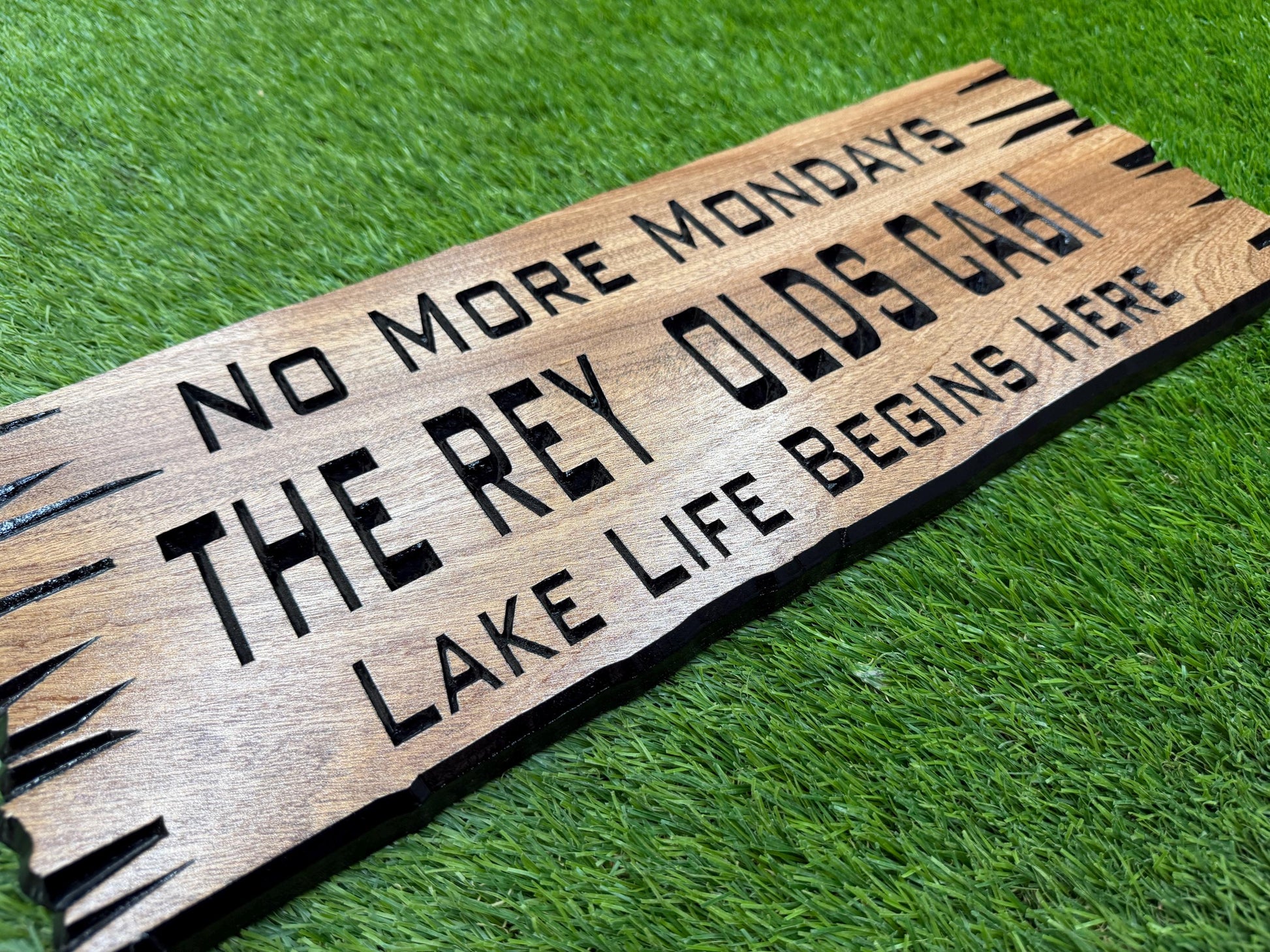 A wooden sign with text on it, placed on a grassy surface.