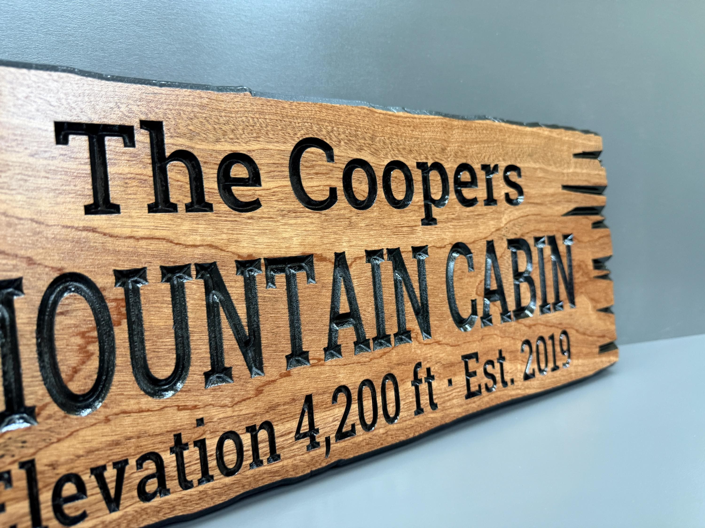 A wooden sign with the text "The Coopers Mountain Cabin" carved into it, indicating the name of the cabin.