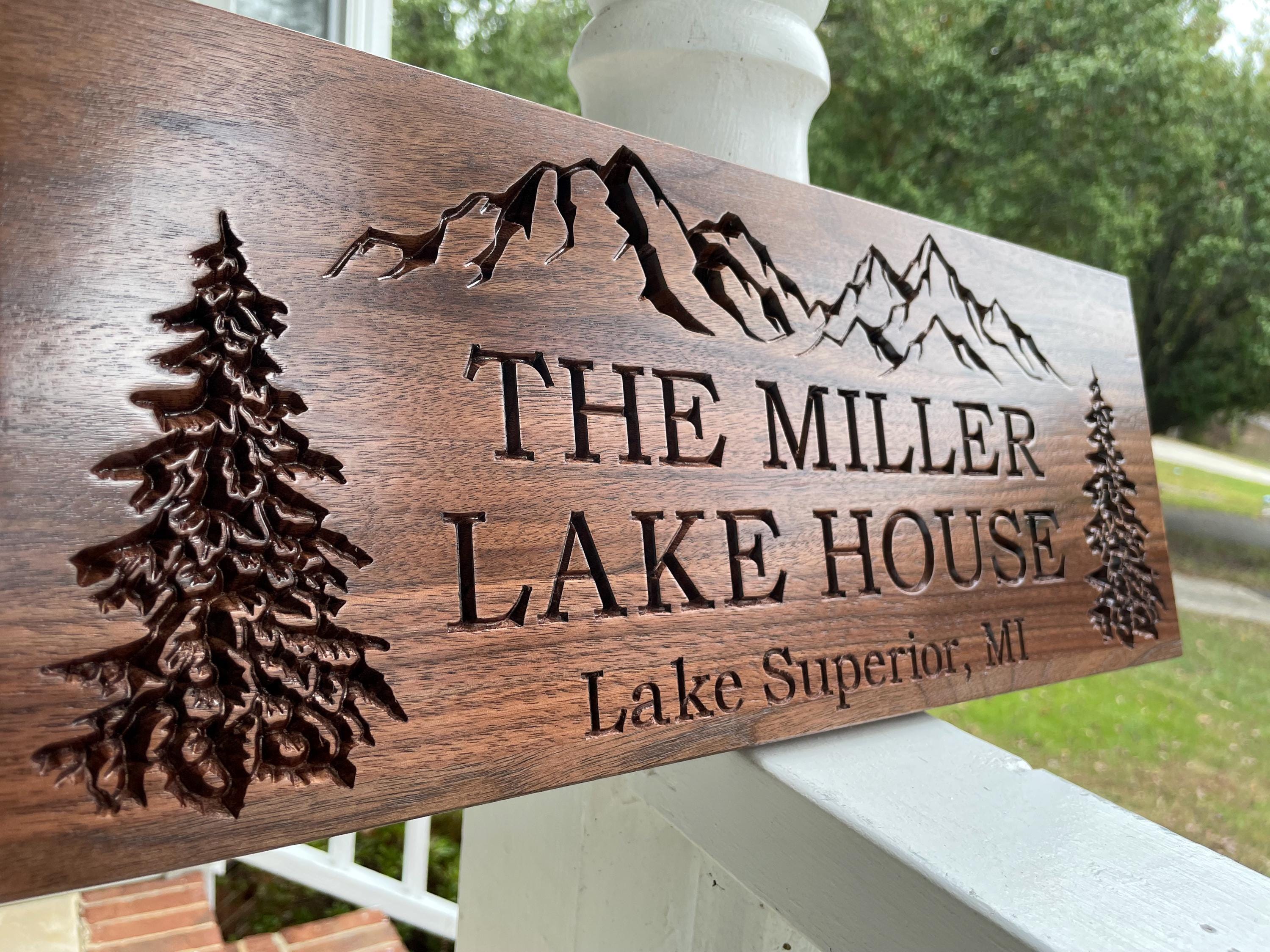 A wooden sign with carved mountain silhouettes and the text "THE MILLER LAKE HOUSE Lake Superior, MI" on it.